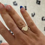 Hand wearing a gold heart-shaped ring with 'LOVE' engraving on a patterned background