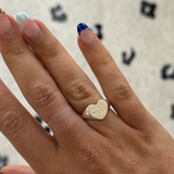 Hand wearing a gold heart-shaped ring with 'LOVE' engraving on a patterned background