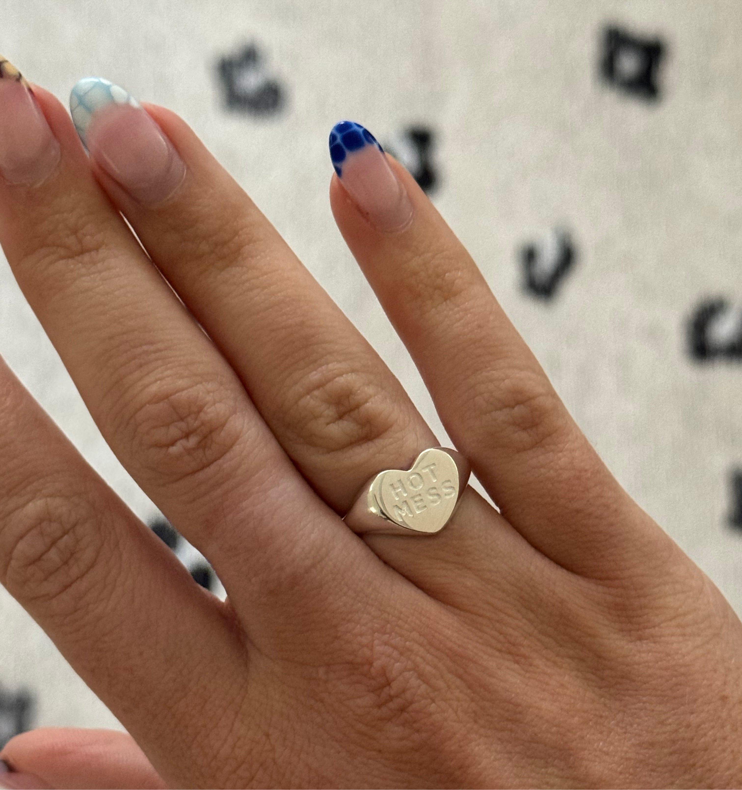 Hand wearing a gold heart-shaped ring with 'LOVE' engraving on a patterned background