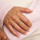 Hand wearing a ring with colorful gemstones on a light pink background