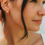 Close-up of a woman wearing a gold necklace with a heart-shaped pendant and gold earrings.