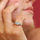 Close-up of a hand wearing a ring with three gemstones against a blurred background