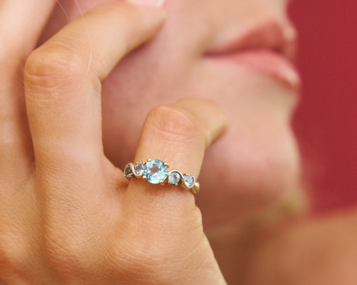 Close-up of a hand wearing a ring with three gemstones against a blurred background