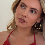 Woman wearing gold hoop earrings and a red top against a neutral background