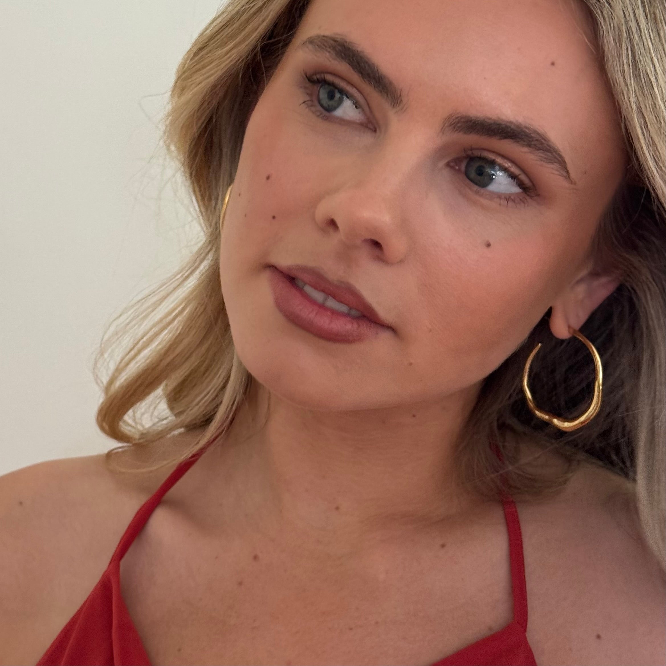 Woman wearing gold hoop earrings and a red top against a neutral background