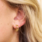 Close-up of a gold heart hoop earring worn by a person with blonde hair.