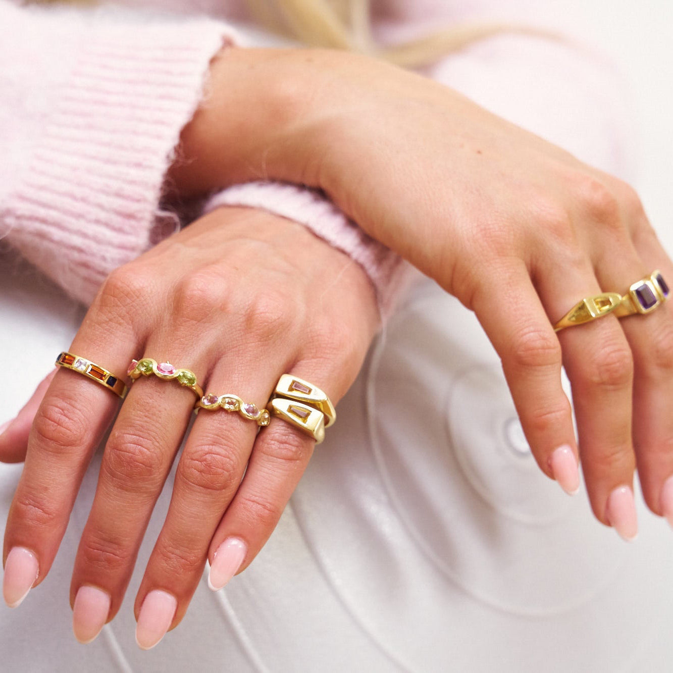 Close-up of hands wearing gold rings on a light background