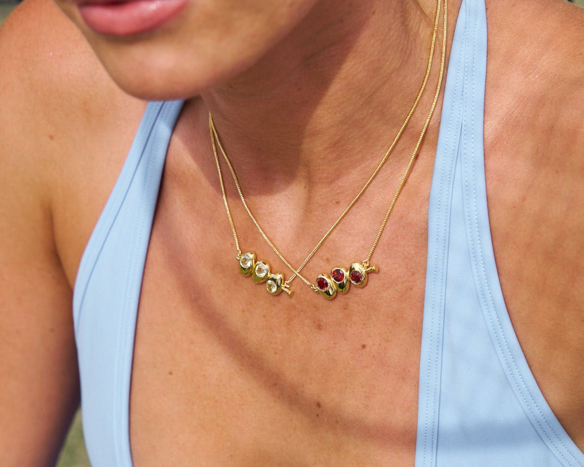 Close-up of a person wearing a light blue tank top and a gold necklace with gemstones.