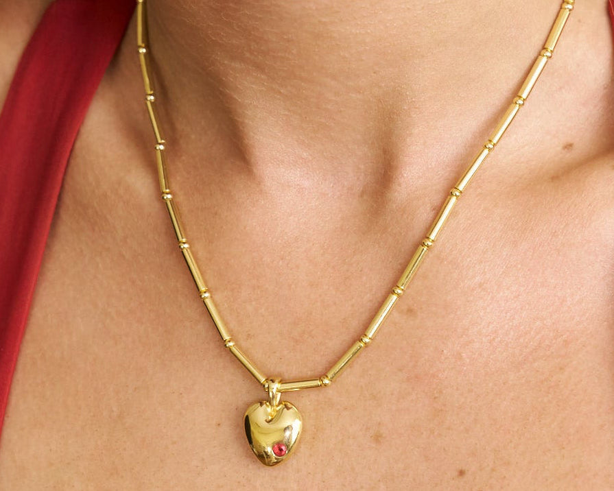 Gold necklace with a heart pendant worn by a person in a red garment.