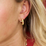 Close-up of a person wearing gold hoop earrings with pink stones.