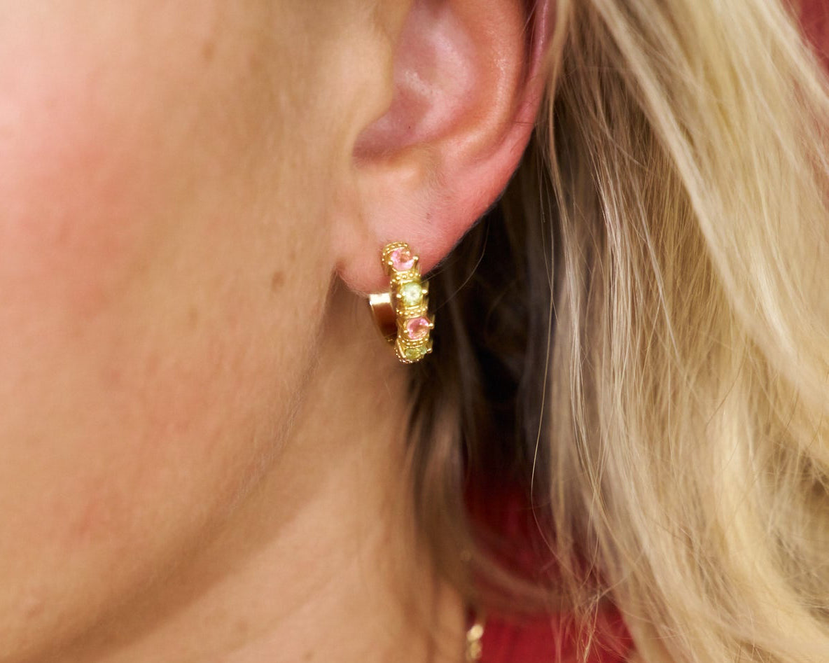 Close-up of a person wearing gold hoop earrings with pink stones.