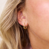 Close-up of a person wearing a square gold hoop earring with blonde hair.
