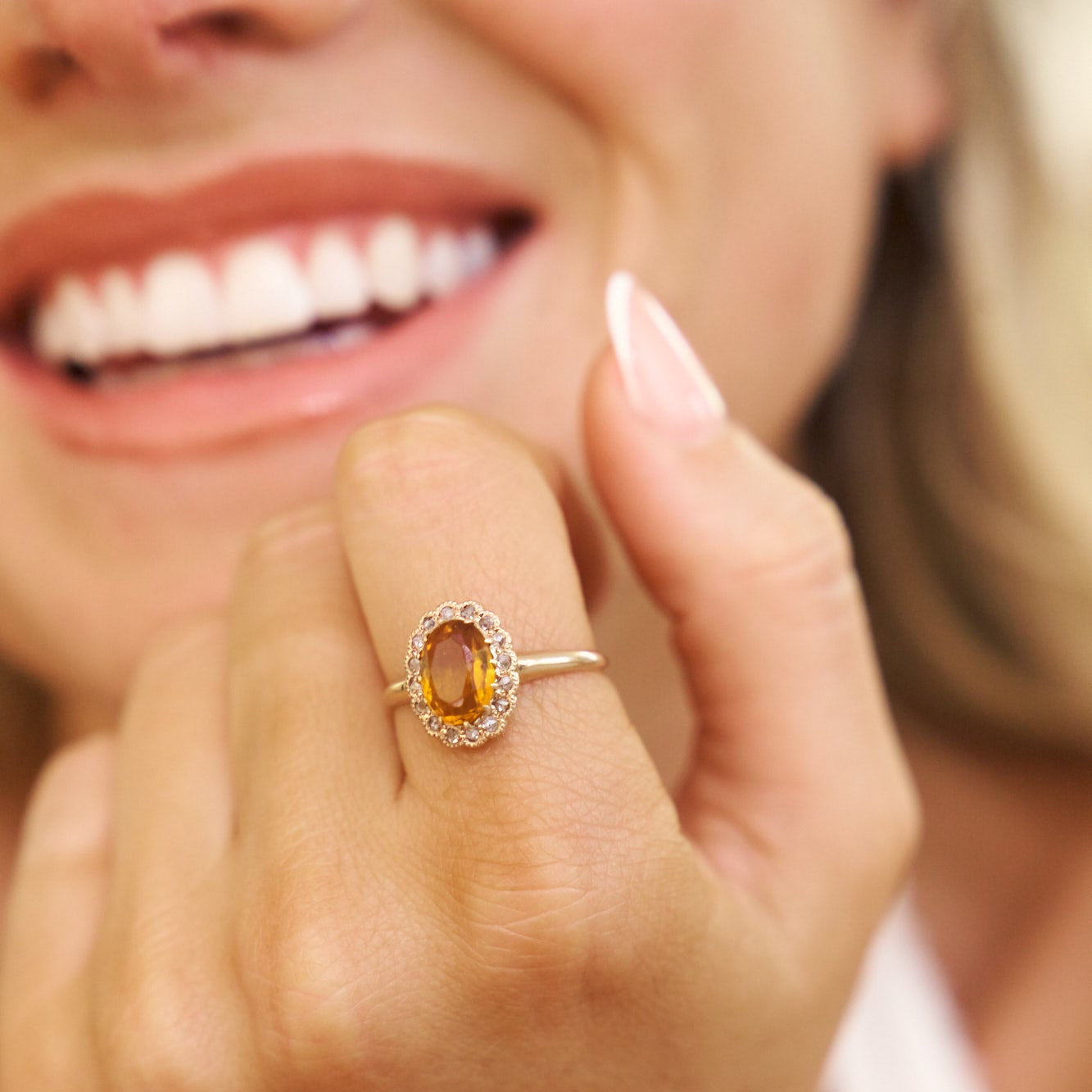 Close-up of a woman's hand wearing a ring with a yellow gemstone, blurred background
