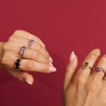 Two hands wearing multiple rings with gemstones against a red background