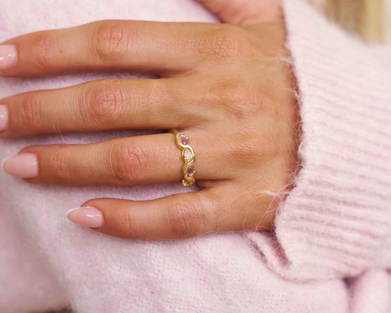 Hand wearing a gold ring with pink background