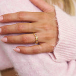 Hand wearing a gold ring with pink background