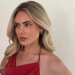 Woman wearing a red top against a plain background with jewellery on