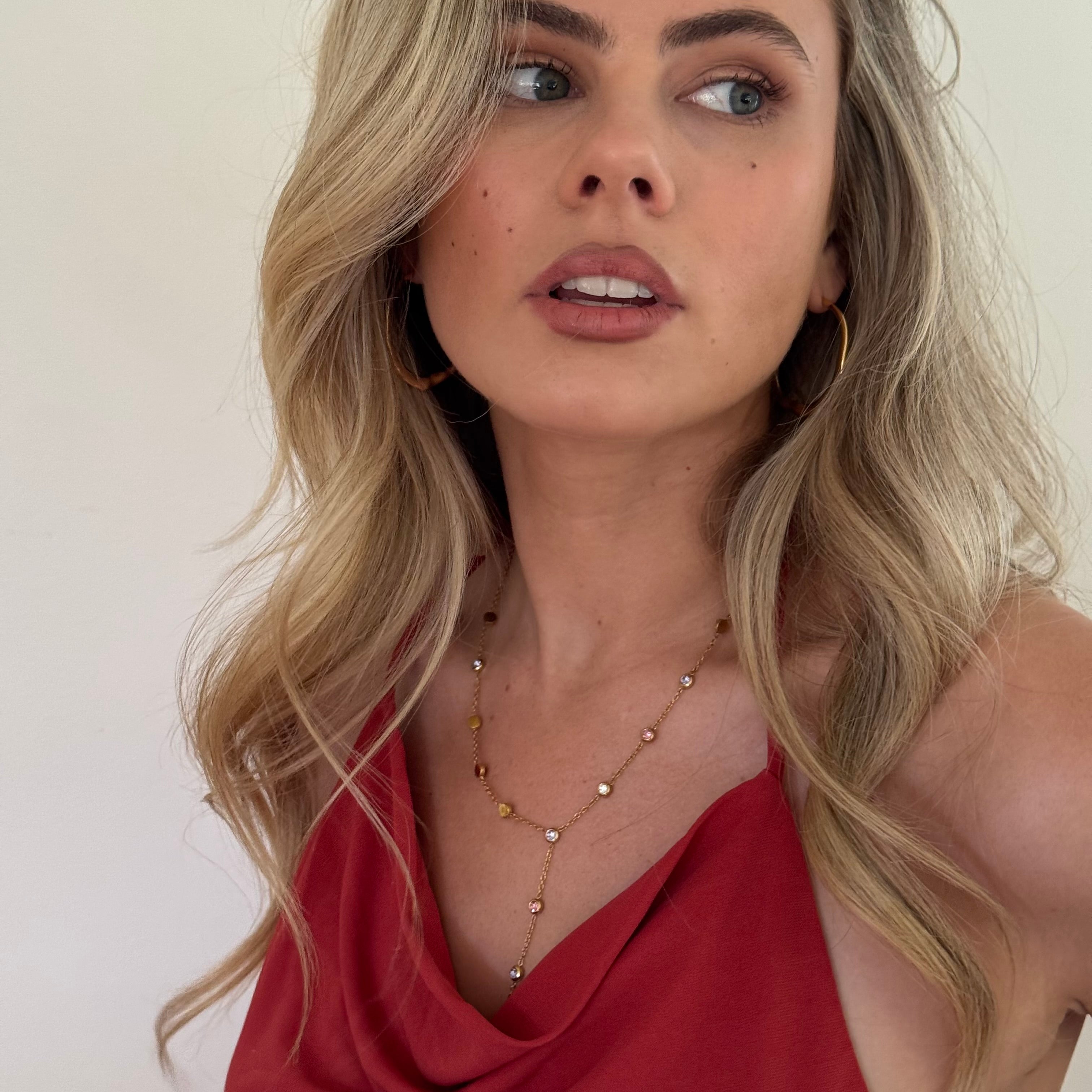 Woman wearing a red top and gold necklace against a plain background