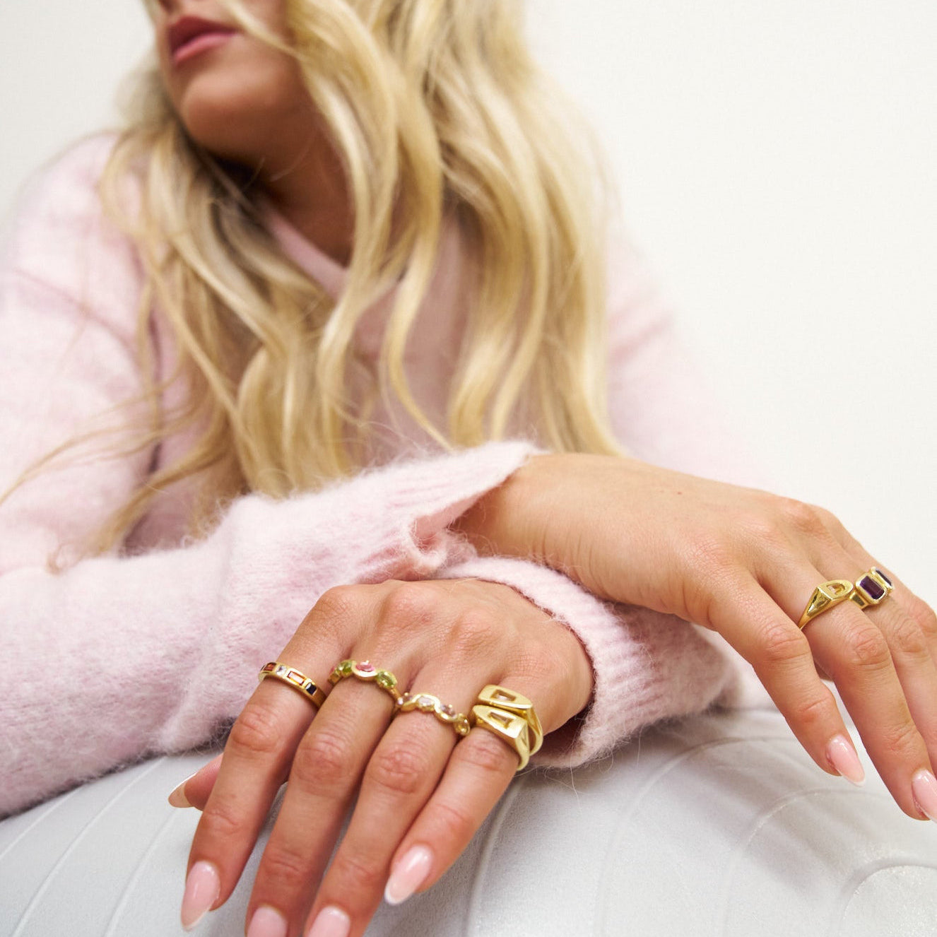 Close-up of a person's hands wearing multiple gold rings with a light background