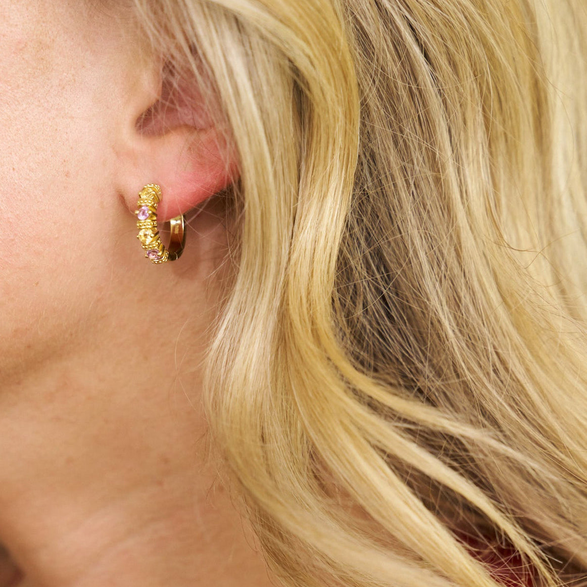 Close-up of a person wearing gold hoop earrings with pink stones.