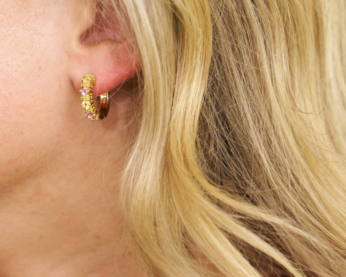 Close-up of a person wearing gold hoop earrings with pink stones.