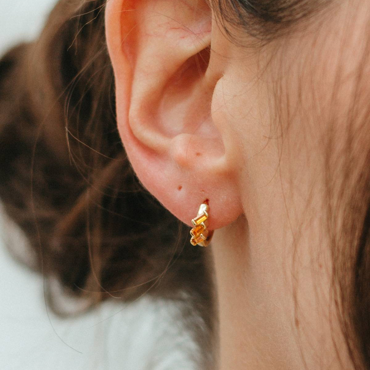 Close-up of an ear wearing a gold earring with a blurred background
