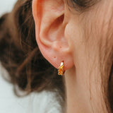 Close-up of an ear wearing a gold earring with a blurred background