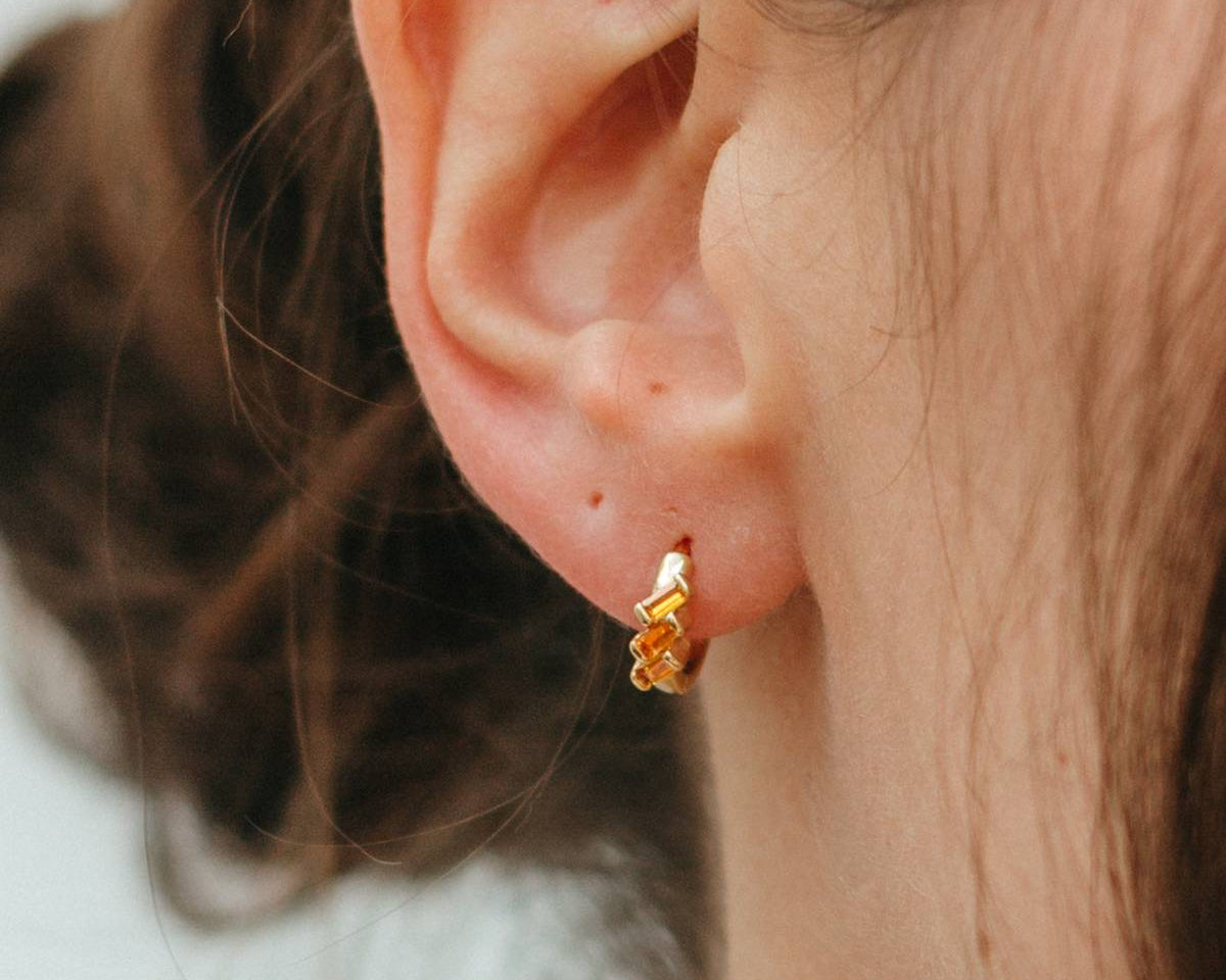 Close-up of an ear wearing a gold earring with a blurred background