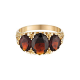 Gold ring with three dark red garnet gemstones on a white background