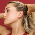 Woman adjusting her hair against a red background wearing Bixby earrings 