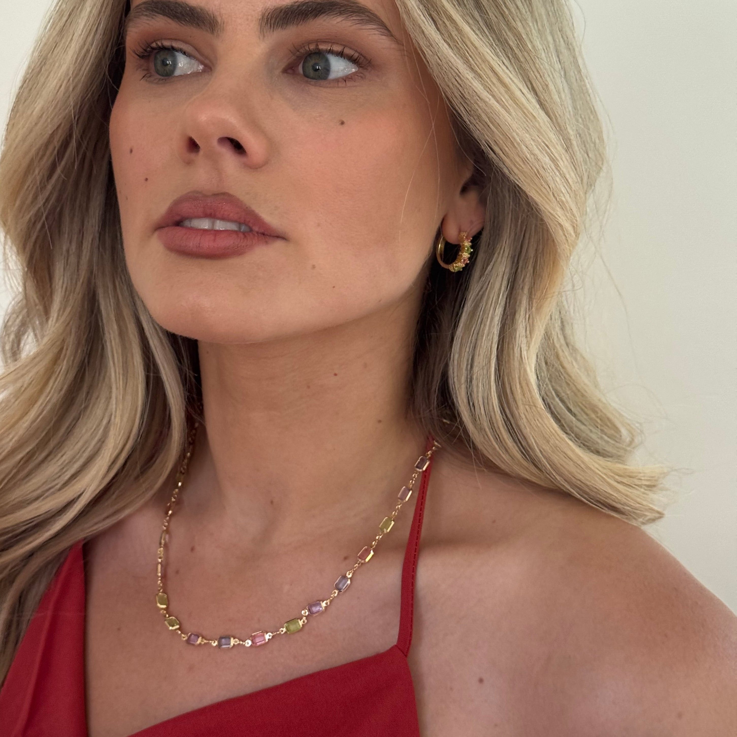Woman with blonde hair and red top against a plain background with colourful earrings on