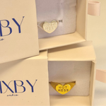 Gold ring with 'HOT MESS' on a heart-shaped band in a 'BIXBY and co' box.