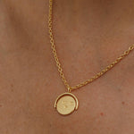 Gold necklace with a round pendant on a person's neck