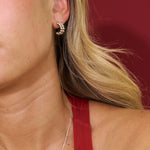 Close-up of a person wearing gold hoop earrings with a blurred red background