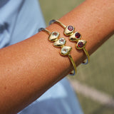 Gold bracelet with gemstones on a wrist against a blurred natural background