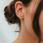 Close-up of an ear wearing a gold earring with a blurred background
