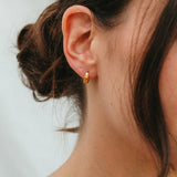 Close-up of an ear wearing a gold earring with a blurred background