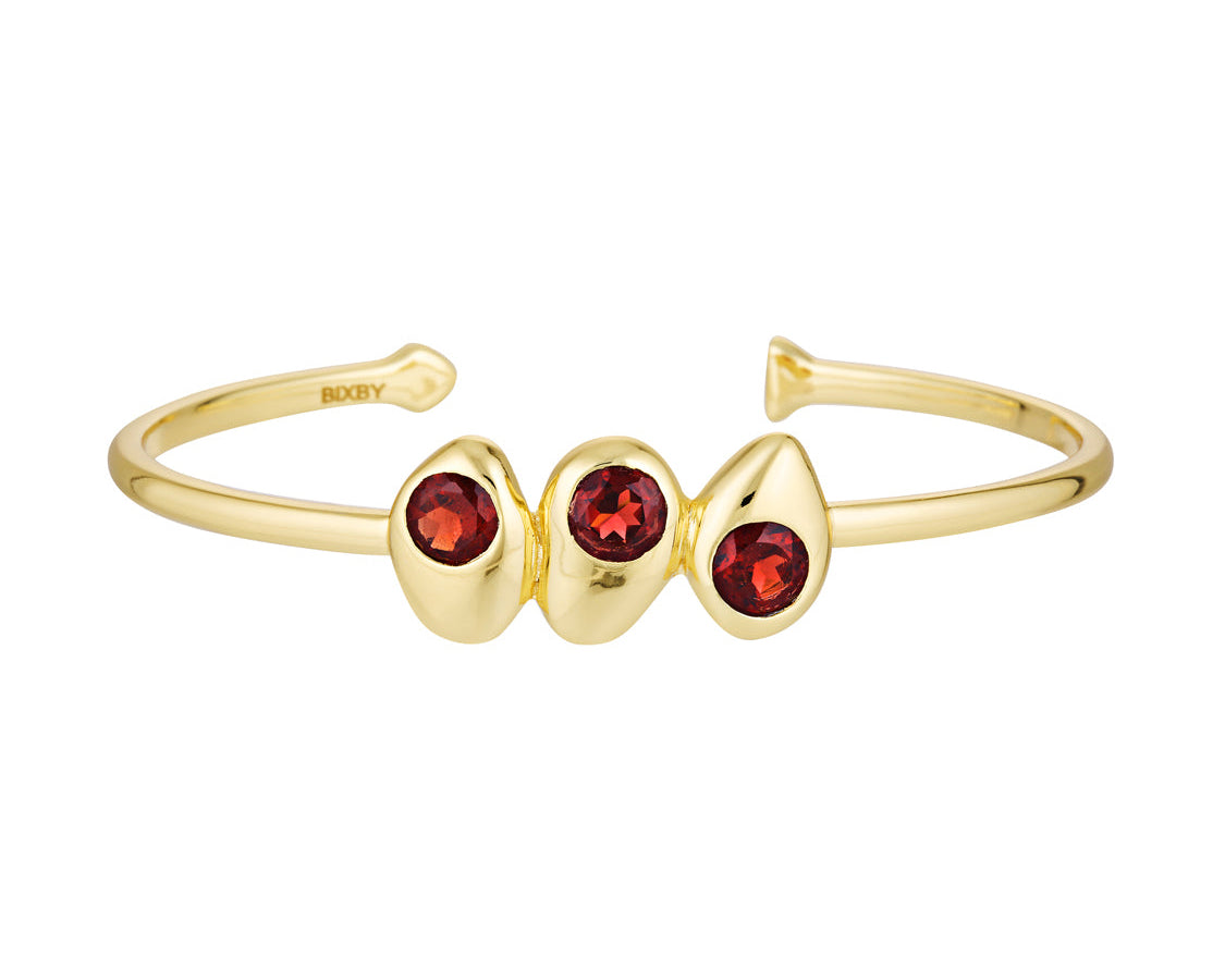Gold bracelet with three red gemstones on a white background