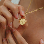 Gold necklace with a round pendant held by hands against a neutral background