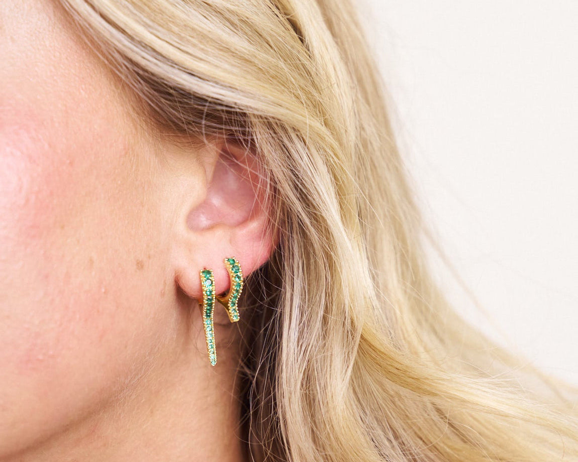 Close-up of a person wearing green gemstone hoop earring stack with a neutral background
