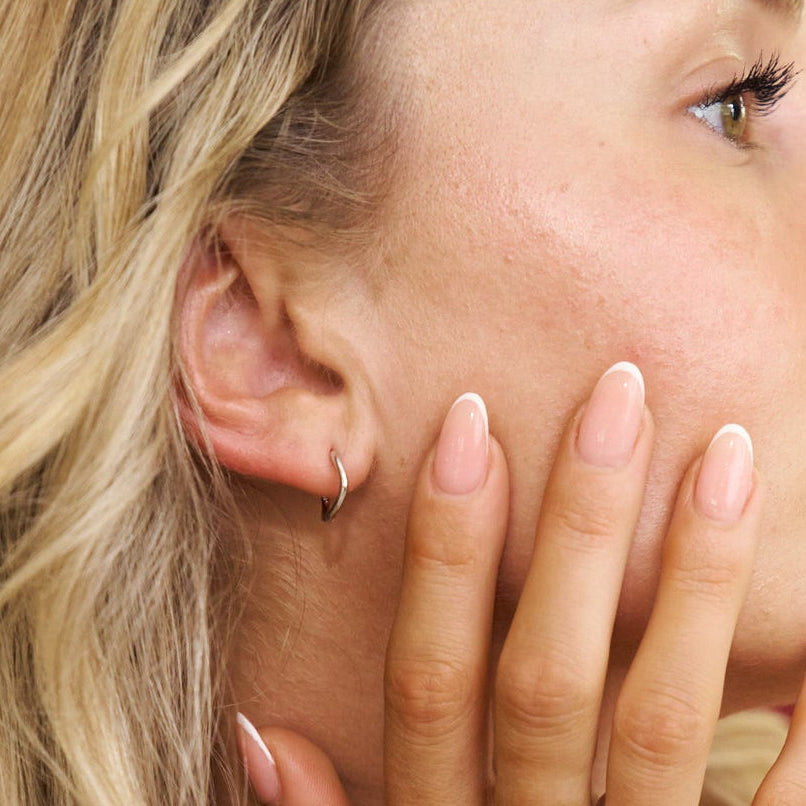 Close-up of a woman's ear with a small hoop earring and hand near her face.