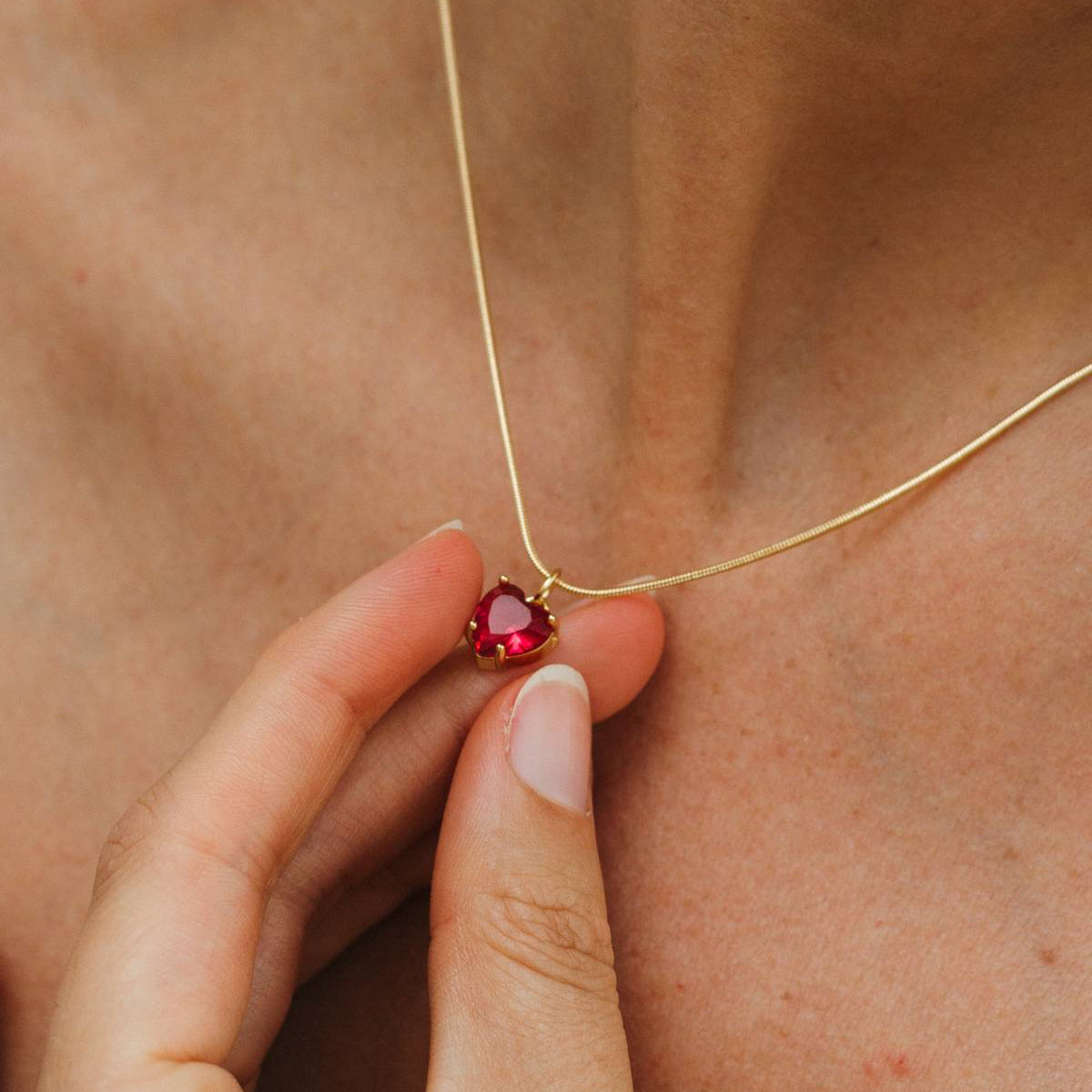 Gold necklace with a red gemstone held against skin