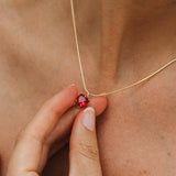 Gold necklace with a red gemstone held against skin