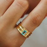 Gold ring with a blue gemstone on a person's finger against a neutral background