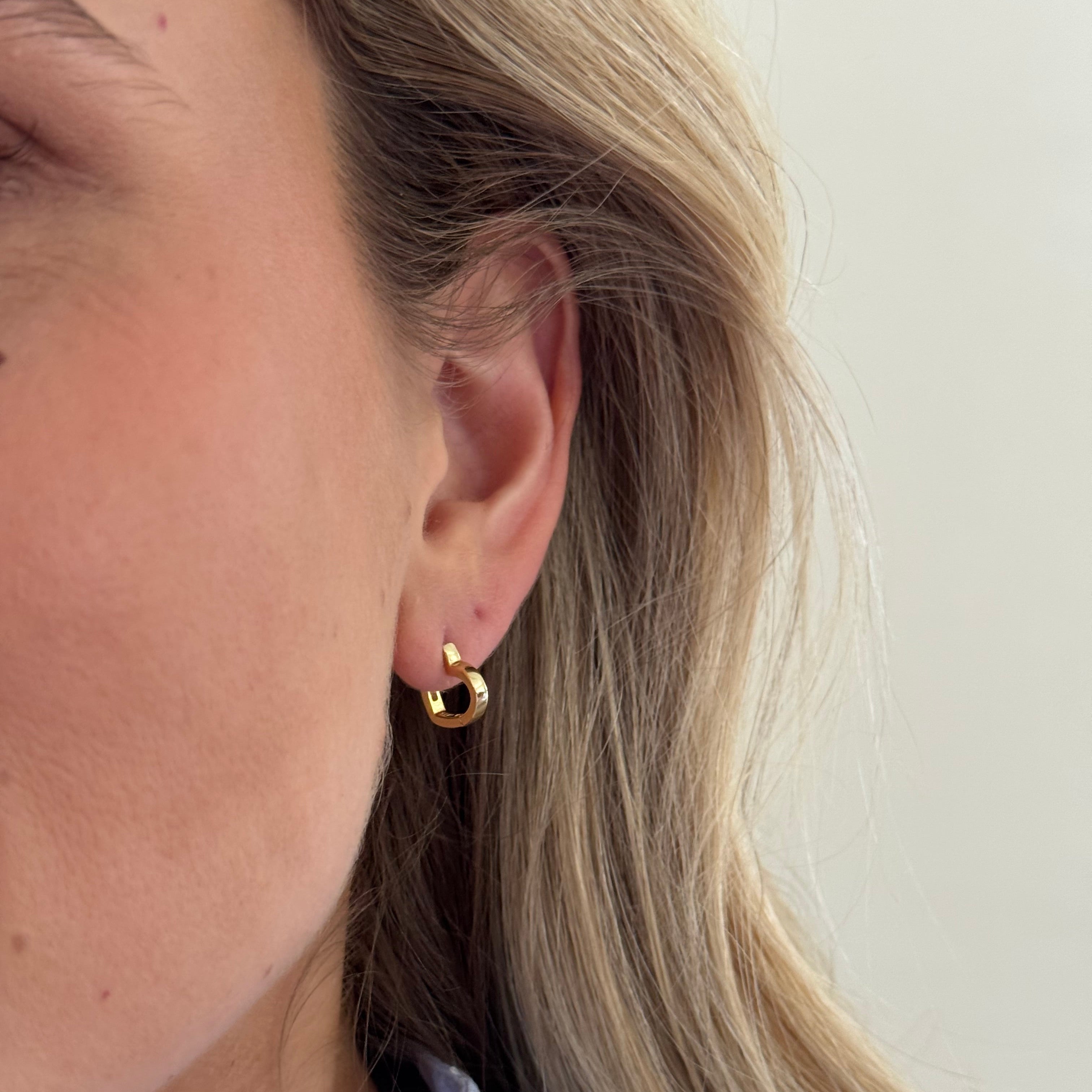 Close-up of an ear wearing a gold earring with a neutral background