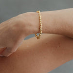 A delicate gold chain bracelet worn on a person's wrist, shown in a close-up shot against a soft gray background.