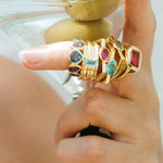 Hand wearing multiple gold rings with gemstones on a blurred background