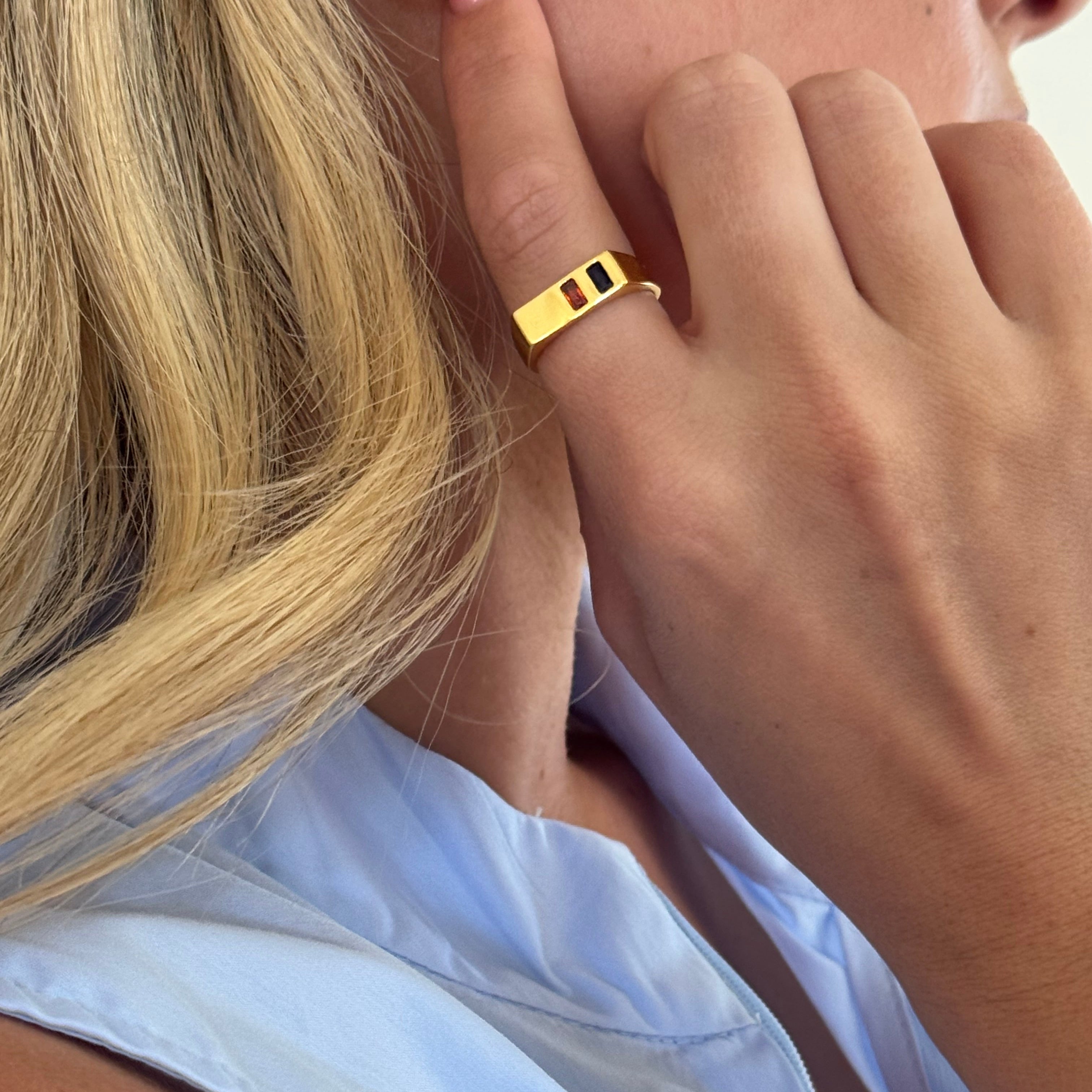 Close-up of a hand wearing a gold ring with a blue garment in the background