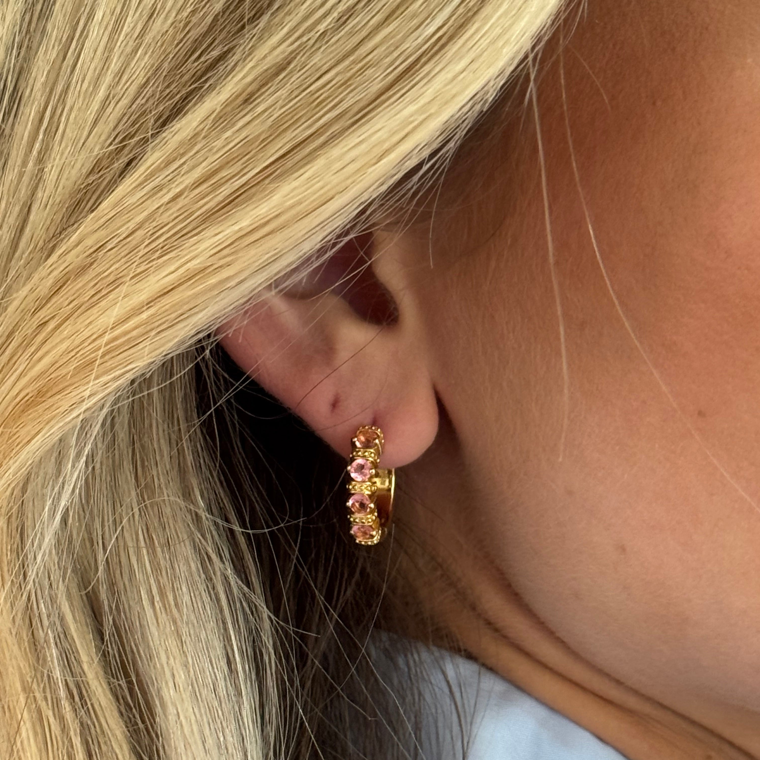 Close-up of an ear wearing a gold earring with pink gemstones.