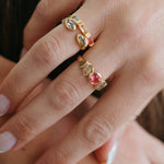 A close-up of a hand wearing two gold rings with marquise-cut clear crystals and one pink heart-shaped crystal.